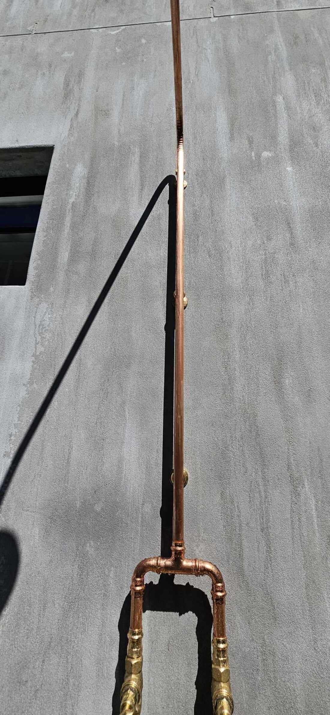 Copper outdoor shower against a concrete wall